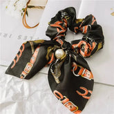 Black silk scrunchie with orange belt pattern and pearl accent, ideal for fashion-forward style